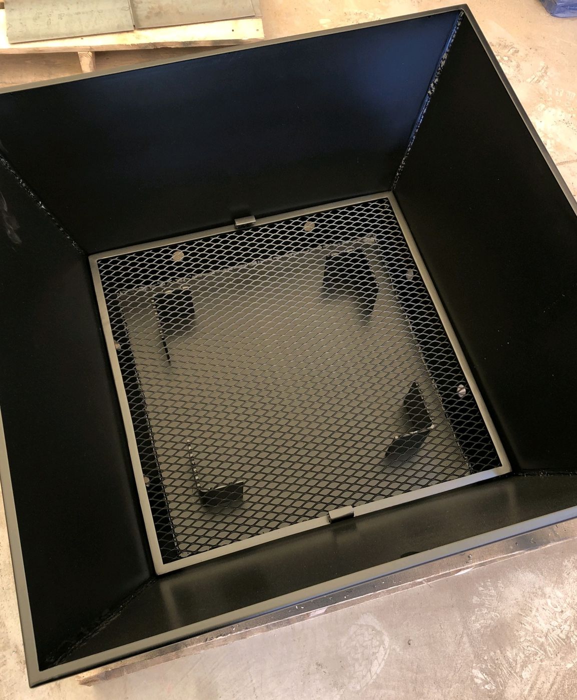 Square steel fire pit with a mesh ember screen and raised grate floor