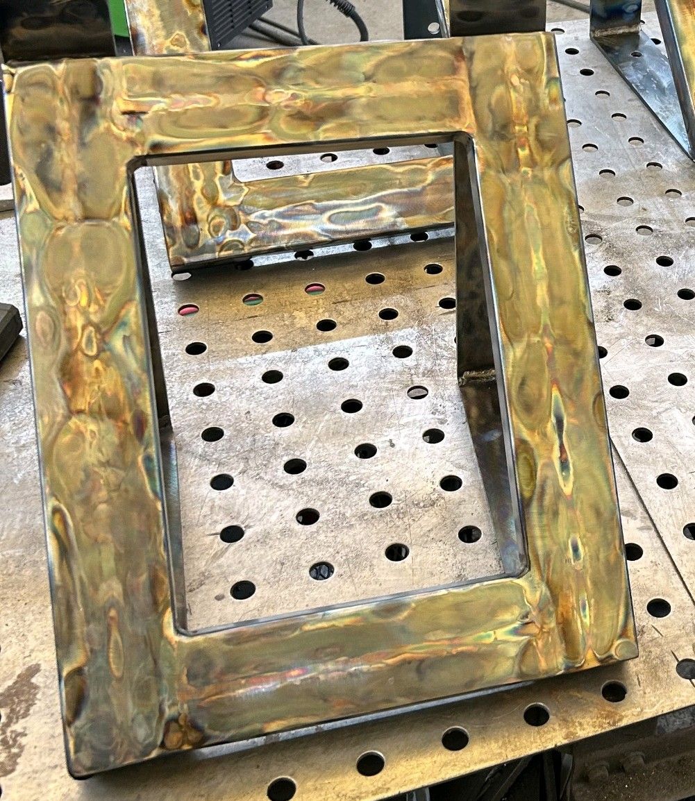 Welded steel rectangular frame with TIG heat-tint colors on a fixture table
