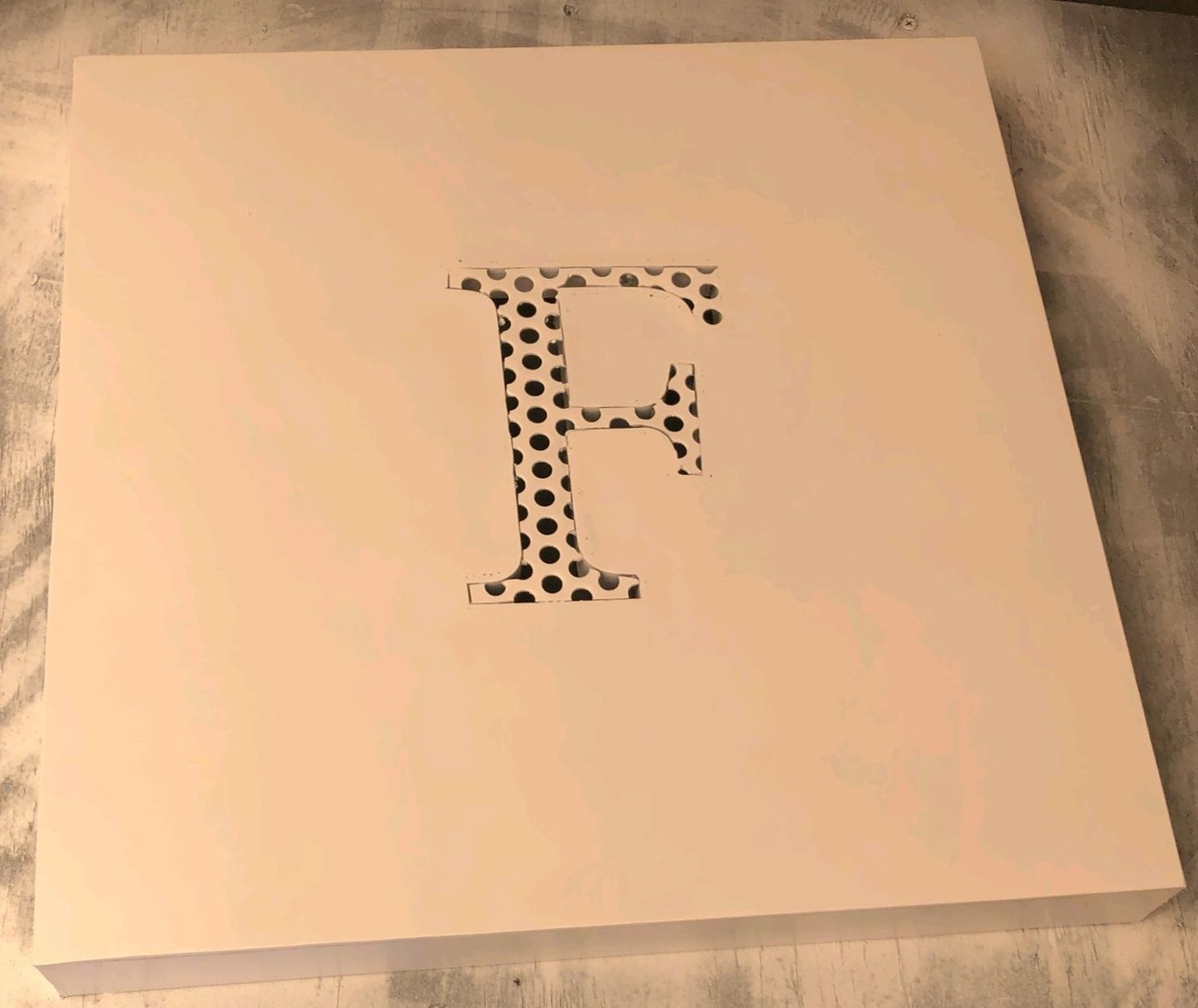 Square steel panel with a cut F monogram