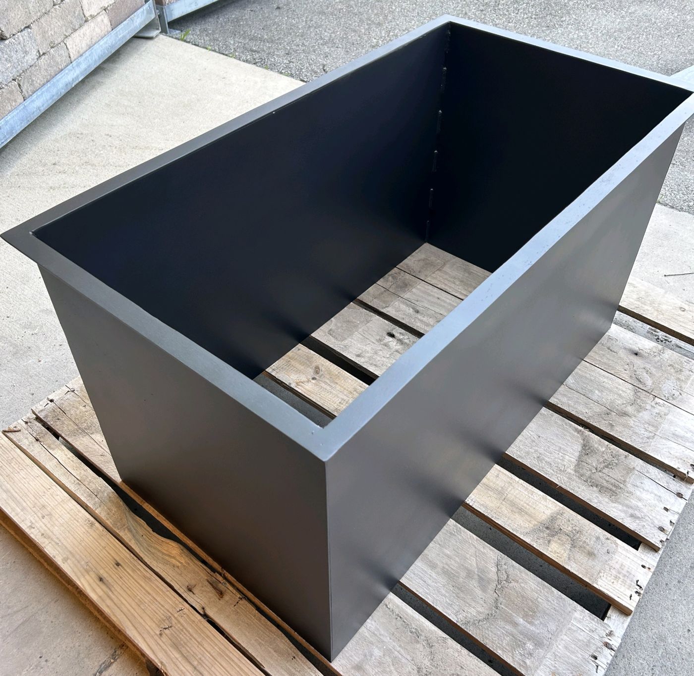 Rectangular steel planter box in dark gray on a pallet